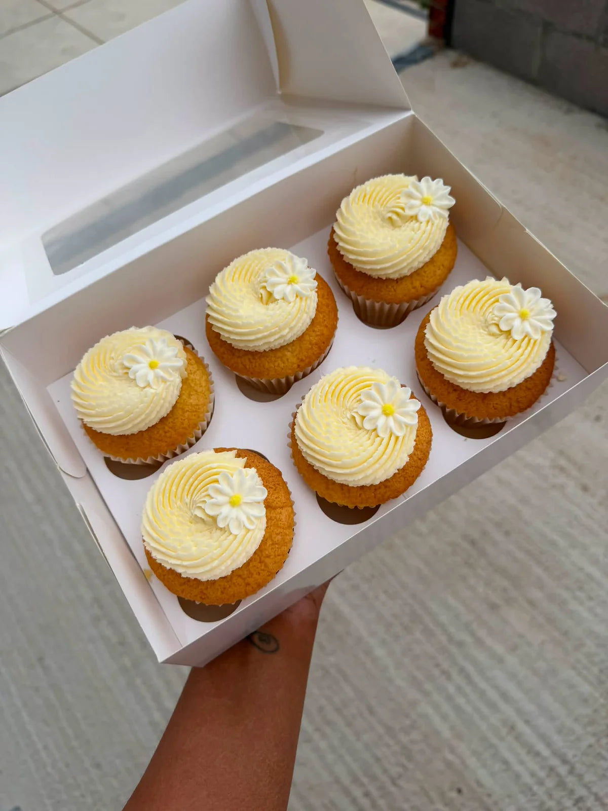 Six lemon cupcakes with buttercream and white flower decorations